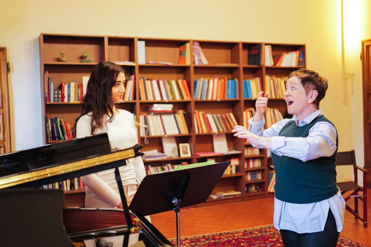 Singing teacher gestures while a young singer stands beside a grand piano in a library room